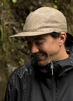 A young man standing in the rain, wearing a waterproof coal cap